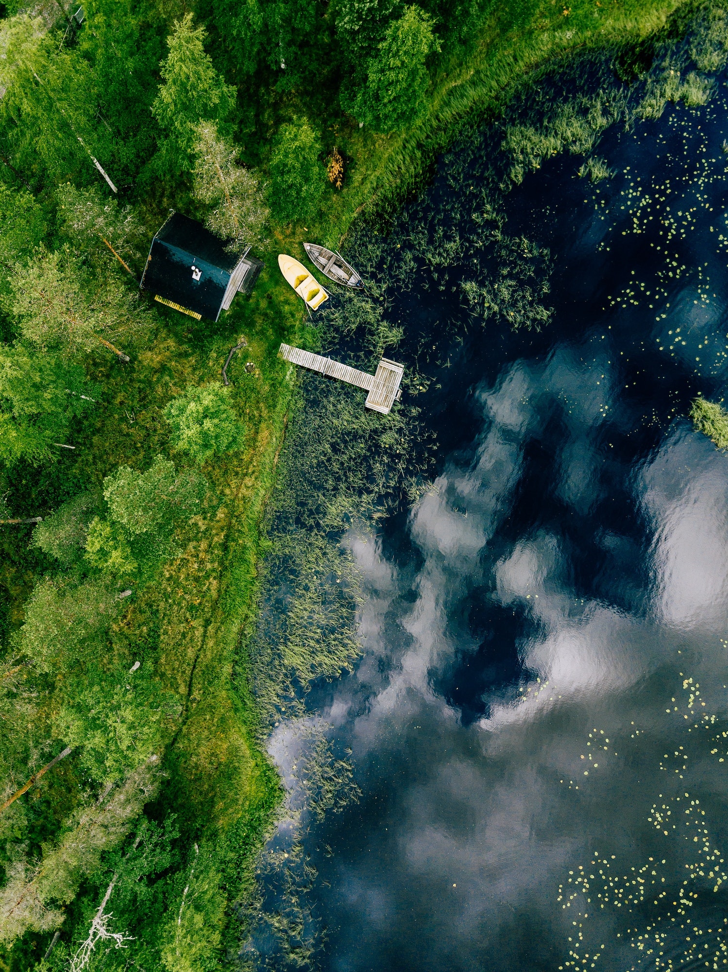 Aerial view of sauna house by the lake shore. Wooden pier with fishing boats.